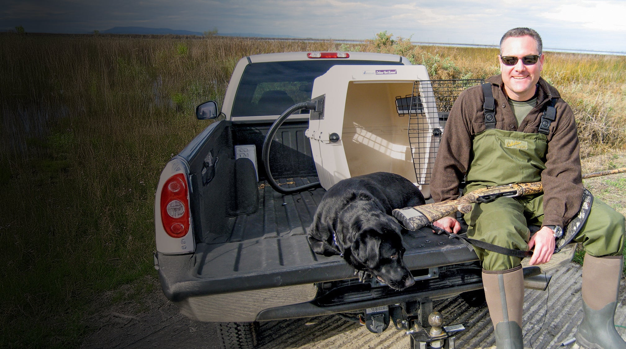 Hunting dog with owner sitting on back of pick up truck near dog crate kept cool using CoolK9 Climate Control System